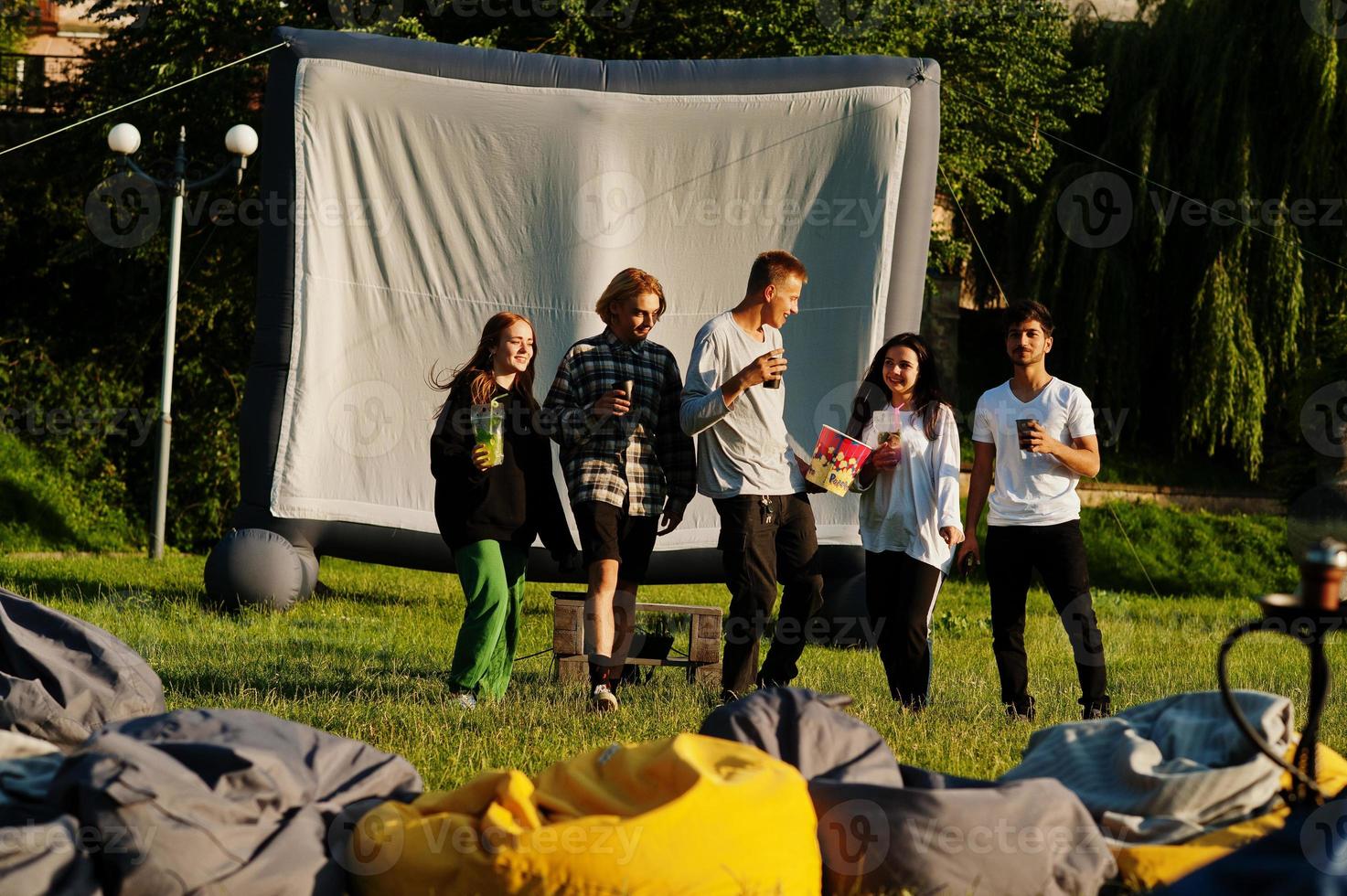 Young multi ethnic group of people watching movie at poof in open air cinema. photo