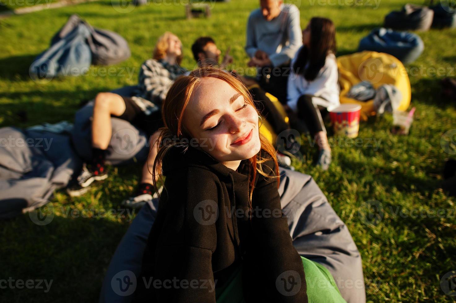 Young multi ethnic group of people watching movie at poof in open air cinema. Close up portrait of funny girl. photo