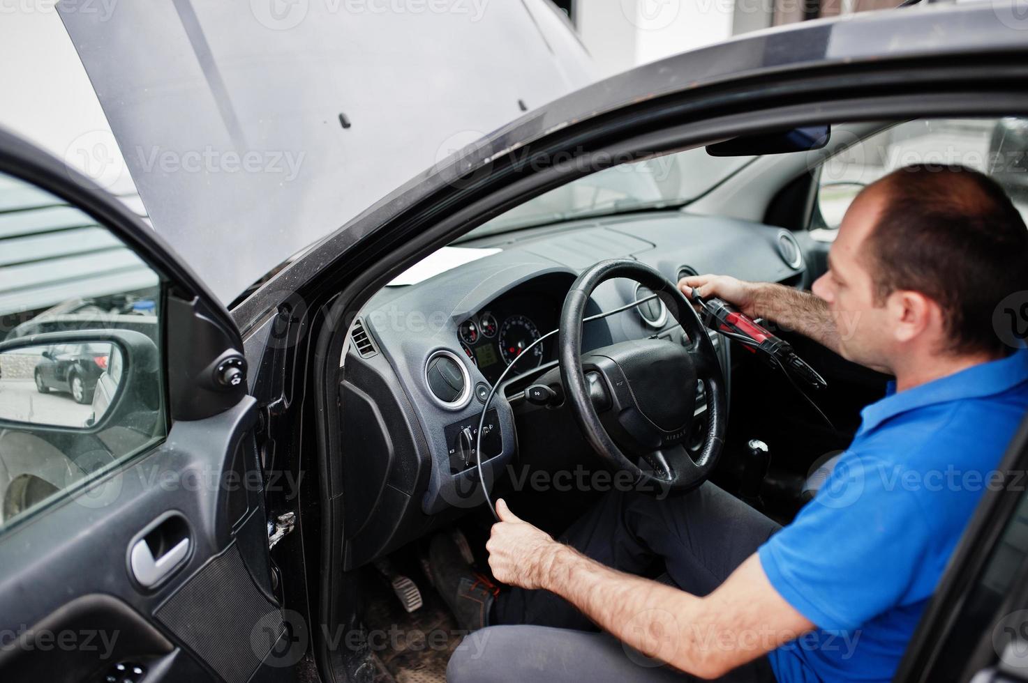 Car repair and maintenance theme. Electric mechanic in uniform working in auto service, making car diagnostics using obd device with laptop. photo