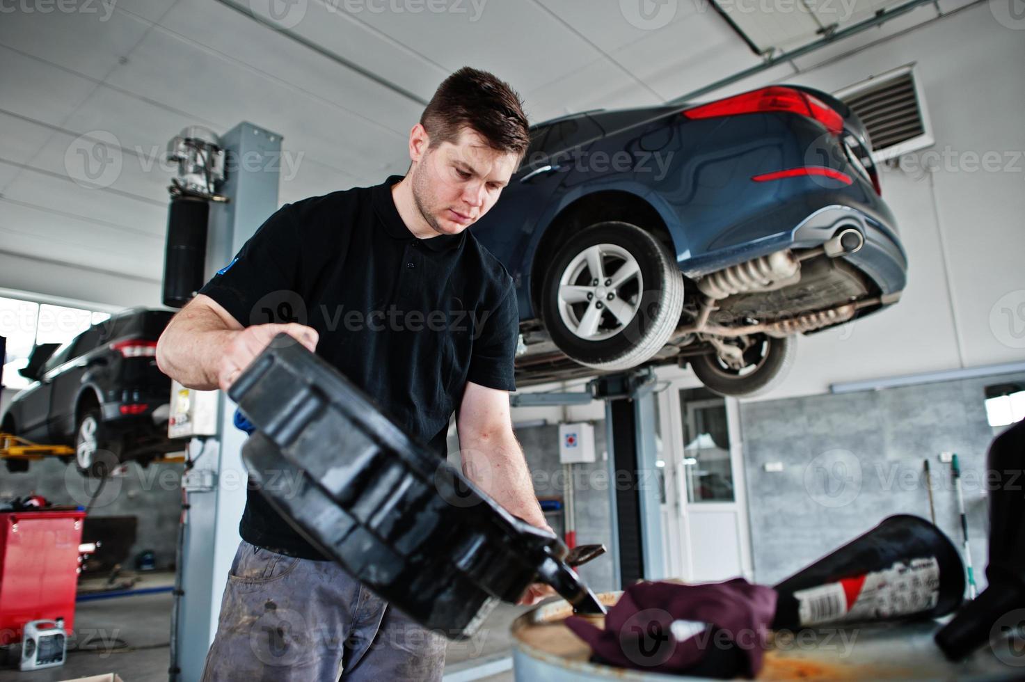 tema de reparación y mantenimiento de automóviles. mecánico en uniforme que trabaja en el servicio de automóviles, vertiendo aceite de motor viejo en el barril. foto