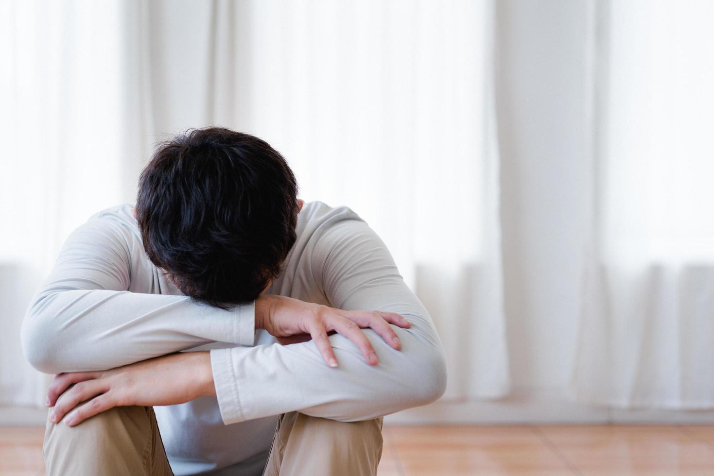 joven asiático deprimido cubriendo la cara con las manos, llorando solo en casa, hombre molesto sentado, sintiéndose infeliz después de una pelea o ruptura, desesperación y soledad y pánico, concepto de problema psicológico foto