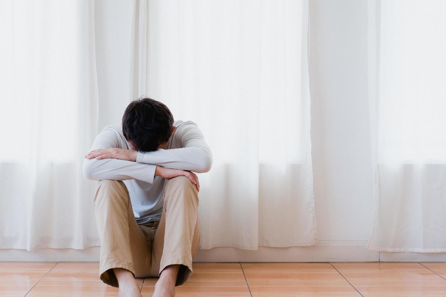 joven asiático deprimido cubriendo la cara con las manos, llorando solo en casa, hombre molesto sentado, sintiéndose infeliz después de una pelea o ruptura, desesperación y soledad y pánico, concepto de problema psicológico foto