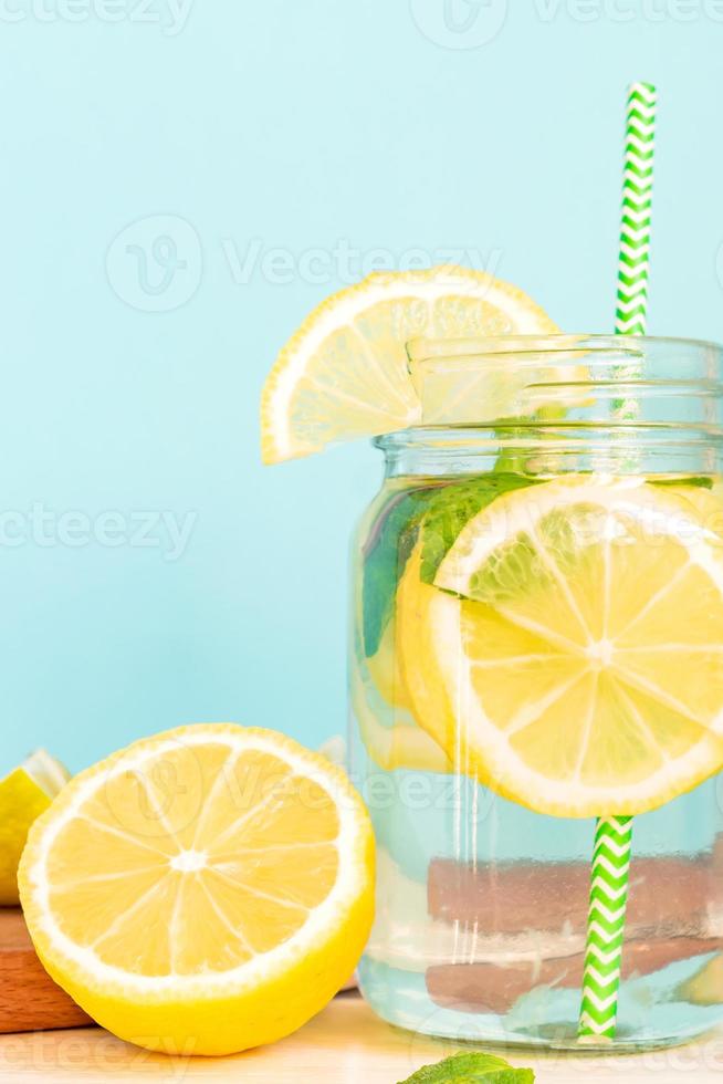Citrus lemonade water with sliced lemon and mint, healthy and detox water drink in summer on wooden table with blue lighten background photo