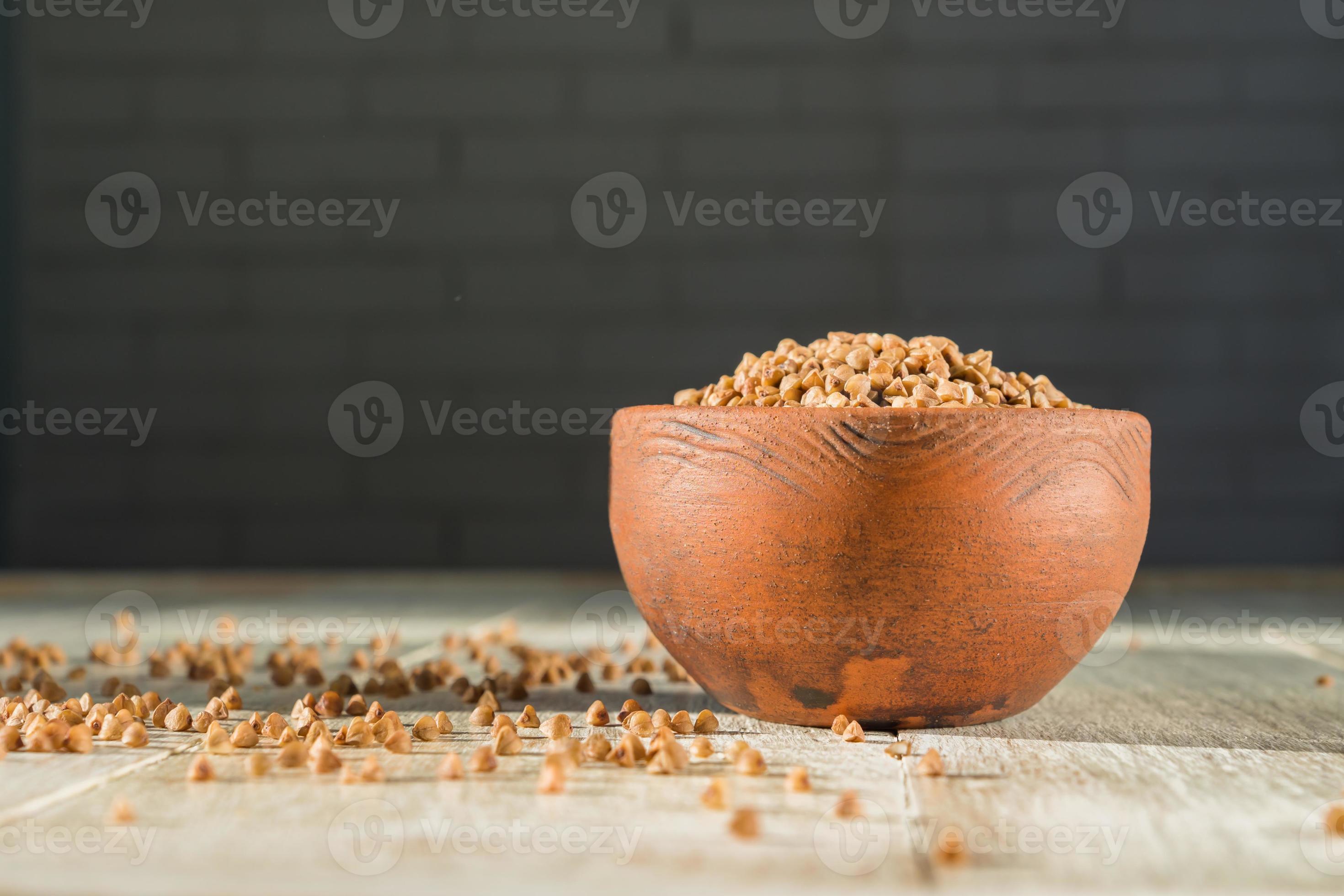 Dry buckwheat in brown clay bowl on wooden table. gluten free grain for