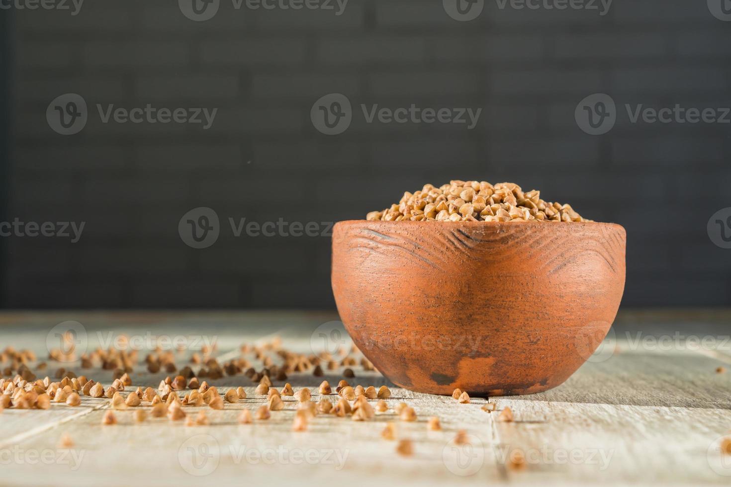Dry buckwheat in brown clay bowl on wooden table. gluten free grain for healthy diet photo