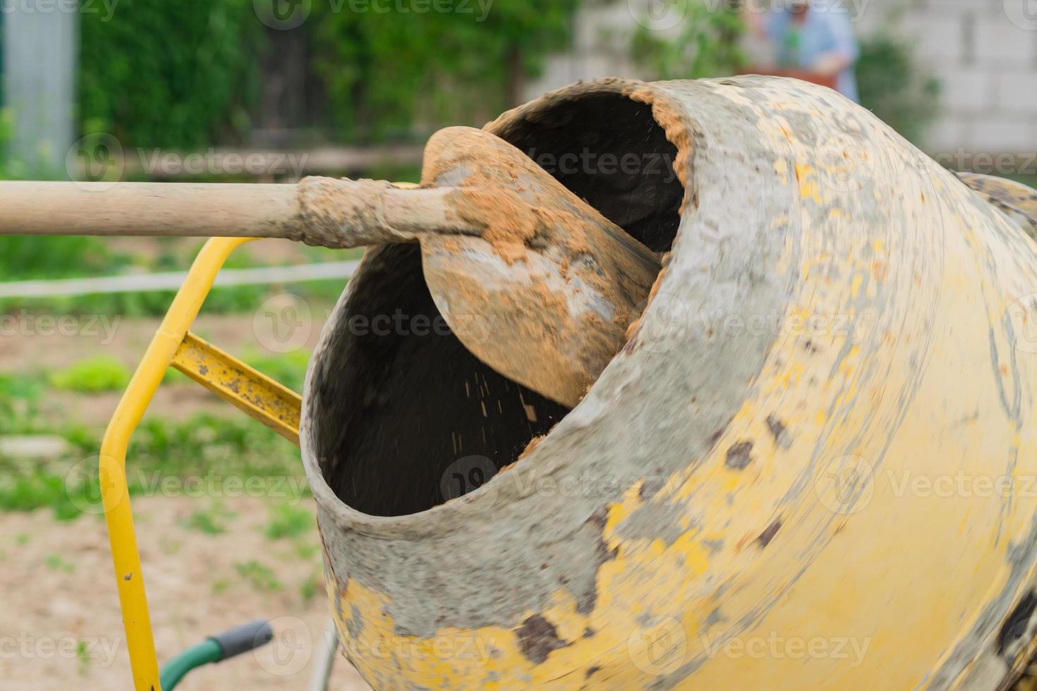 trabajador de la construcción palea la arena en una hormigonera giratoria. proceso de creación de cemento en el sitio de construcción foto