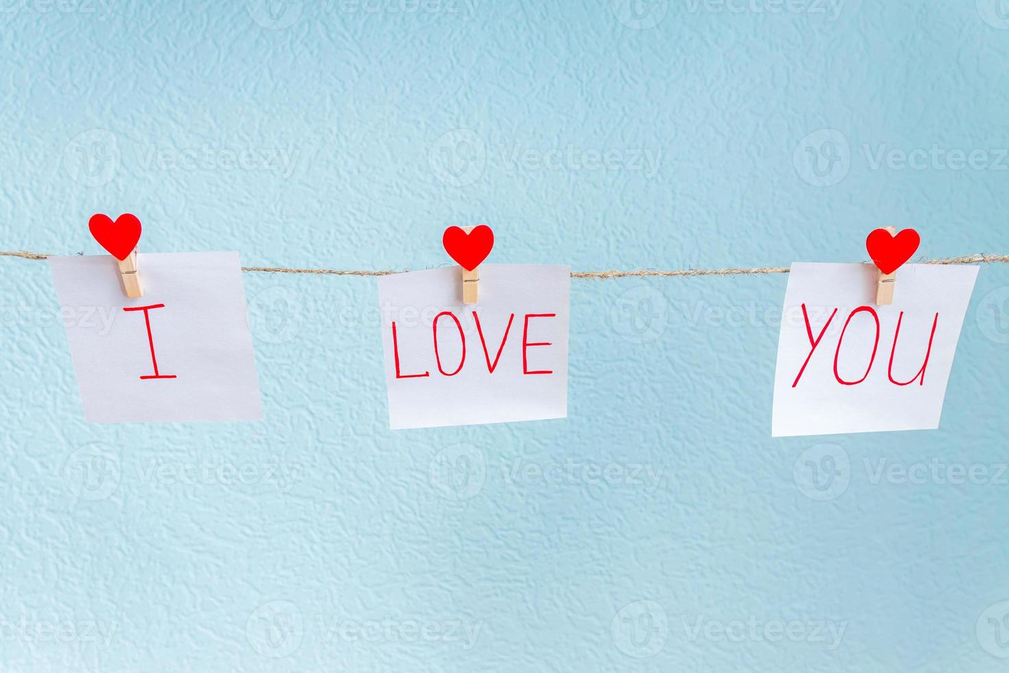 Red Valentine's love hearts pins hanging on natural cord against blue background. I love you inscription on paper pieces. photo