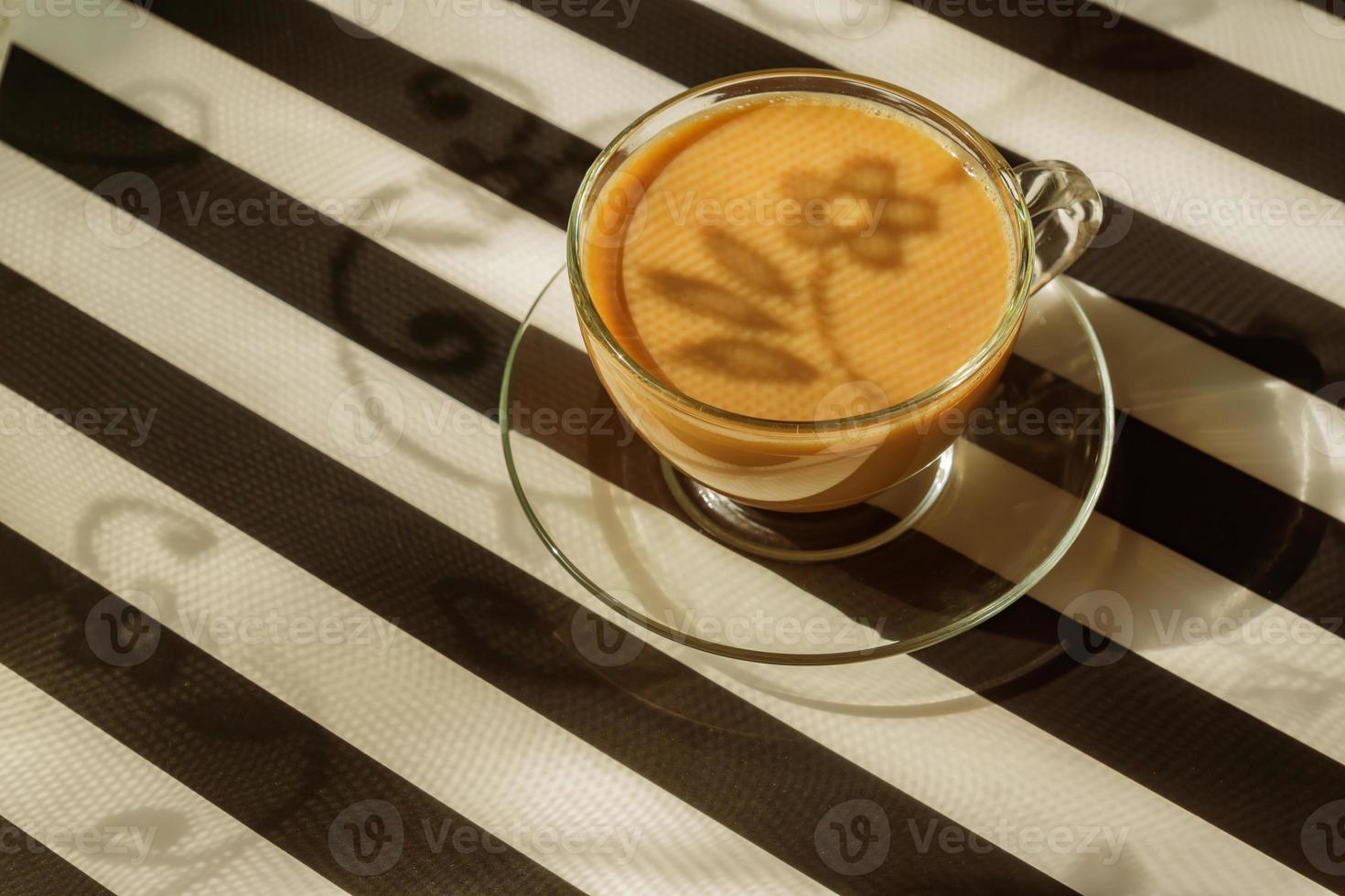 transparent cup of creamy coffe on dark background. Sunlight and hard shadows. Toned image with copy space photo