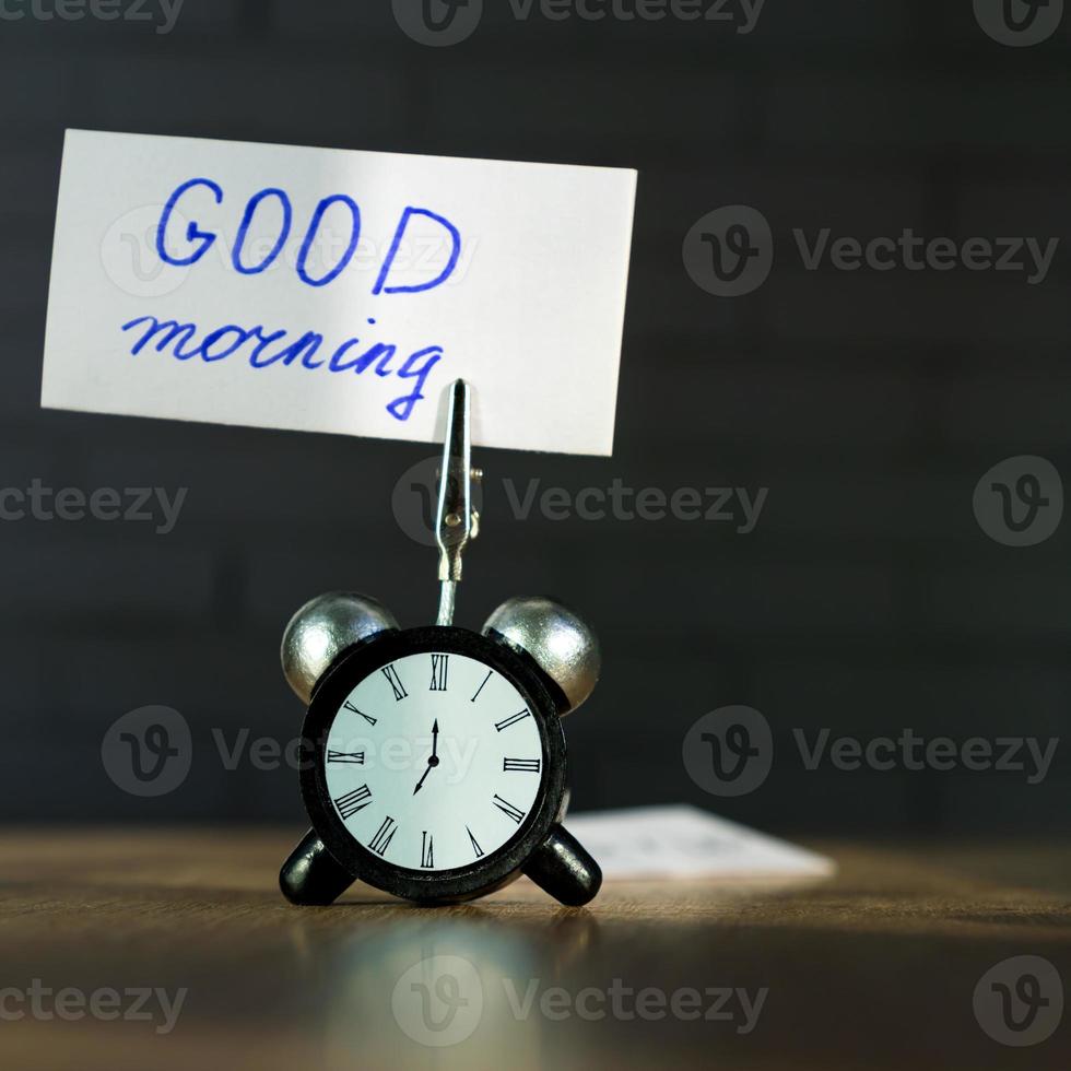 Alarm clock and banner with handwritten phrase good morning on wooden table. Time management concept. photo