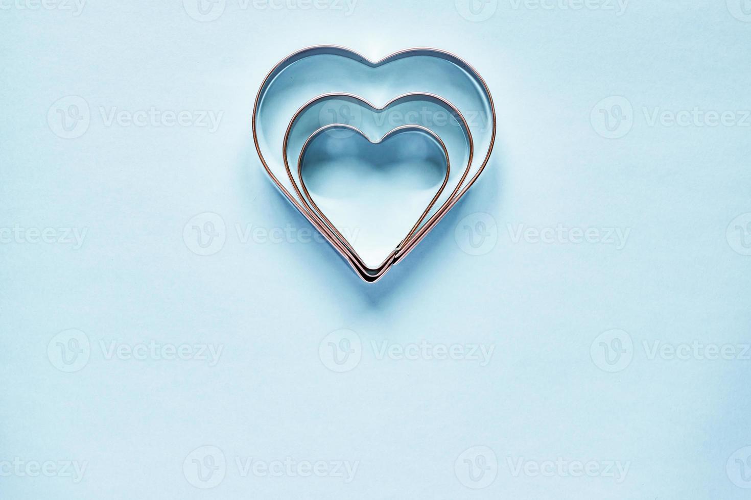 Three metal cookie cutters in heart shape on light blue background with copy space photo