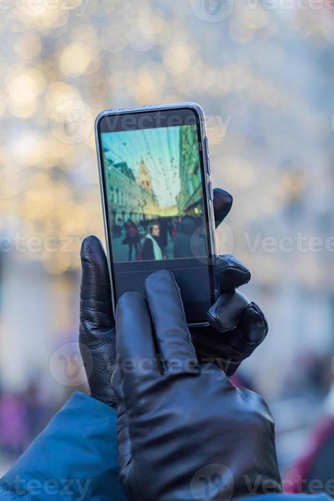 tourist taking picture of a woman in christmas city in a sunny winter day on smartphone camera. Bokeh background photo