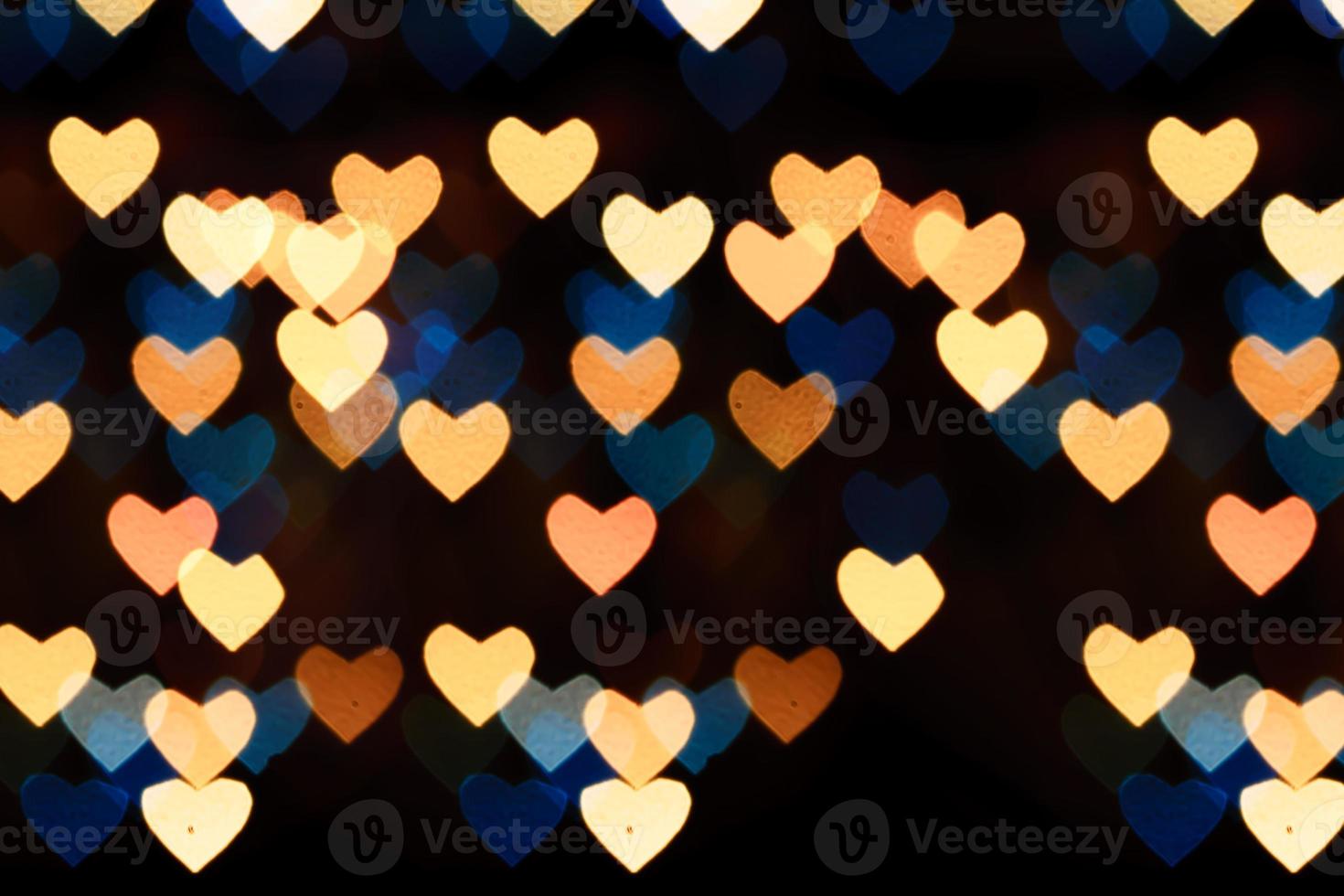 Bokeh de corazones multicolores de colores azul y naranja sobre fondo negro. textura para vacaciones foto