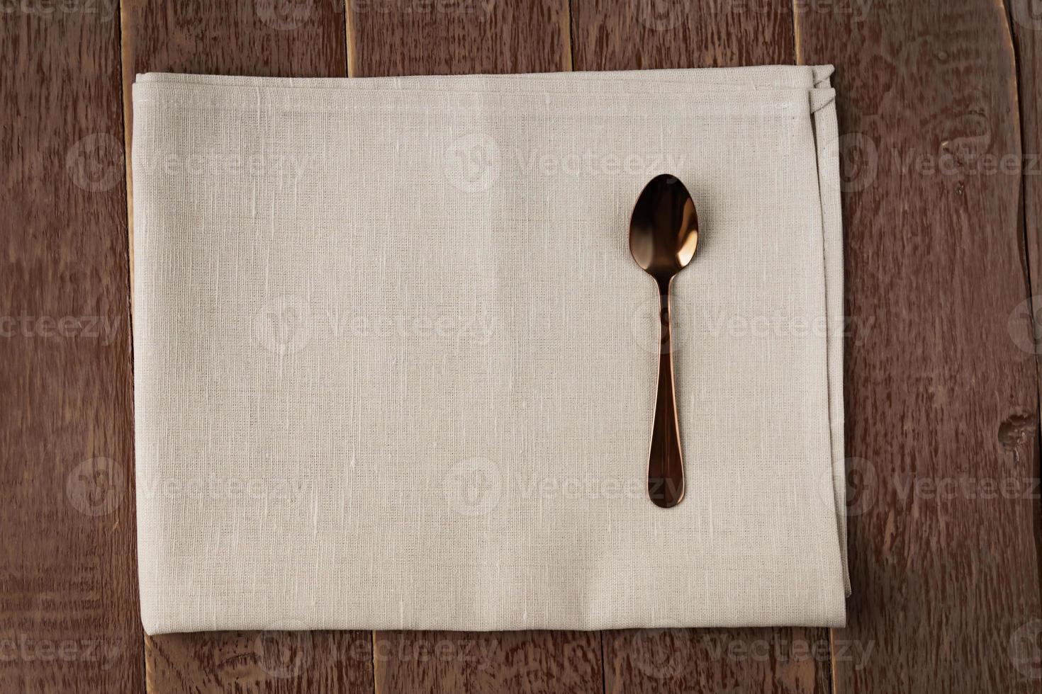 Top view of cloth napkin of beige color and served tea spoon on wooden table. photo
