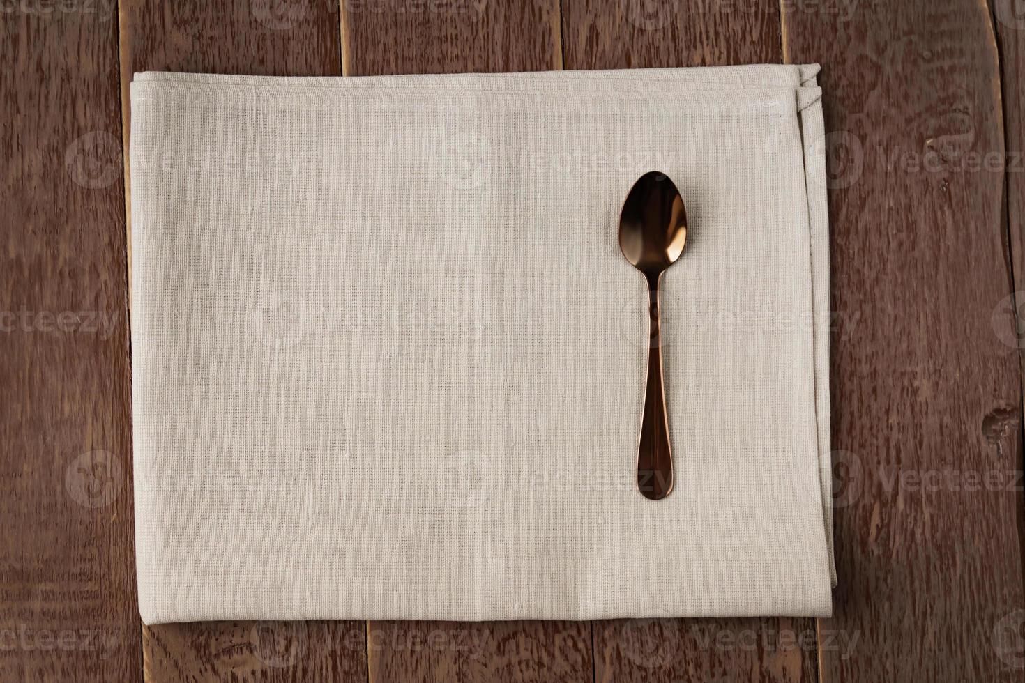 Top view of cloth napkin of beige color and served tea spoon on wooden table. photo