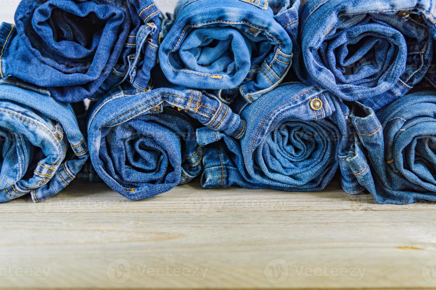 top view of roll blue denim jeans arranged in stack on wooden shelf. Beauty and fashion clothing concept photo