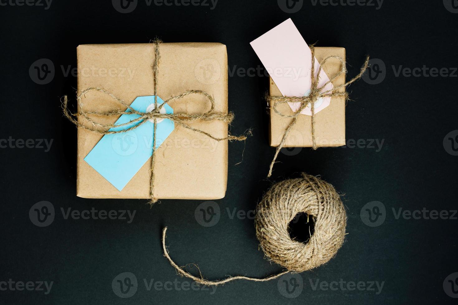 Handcrafted gift box wrapped in Craft paper with red wooden heart, rope and bow on black background. Top view, flat lay photo