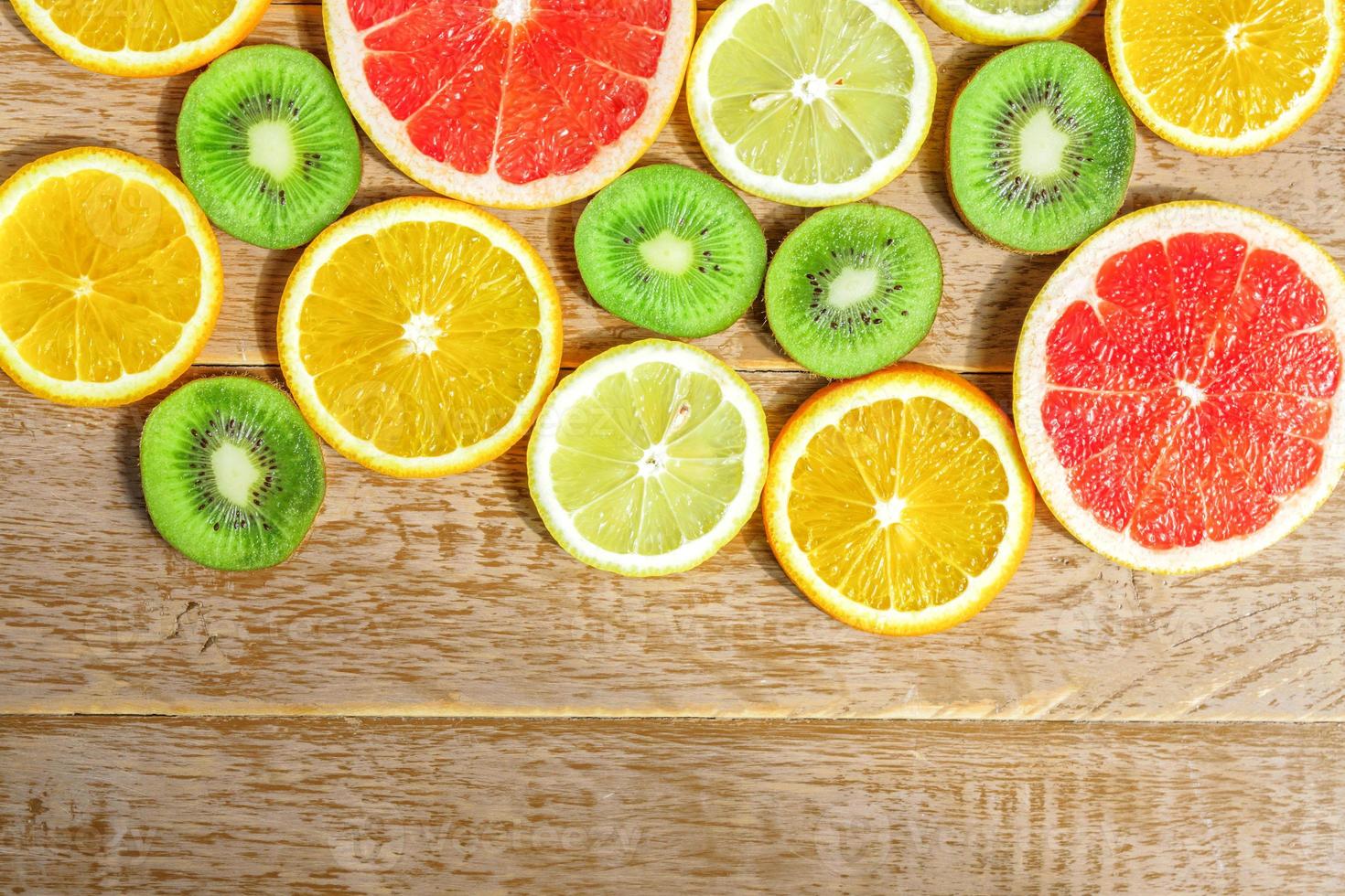frame with slice of oranges, lemons, kiwi, grapefruit pattern on wooden background. Flat lay, top view with copy space. photo