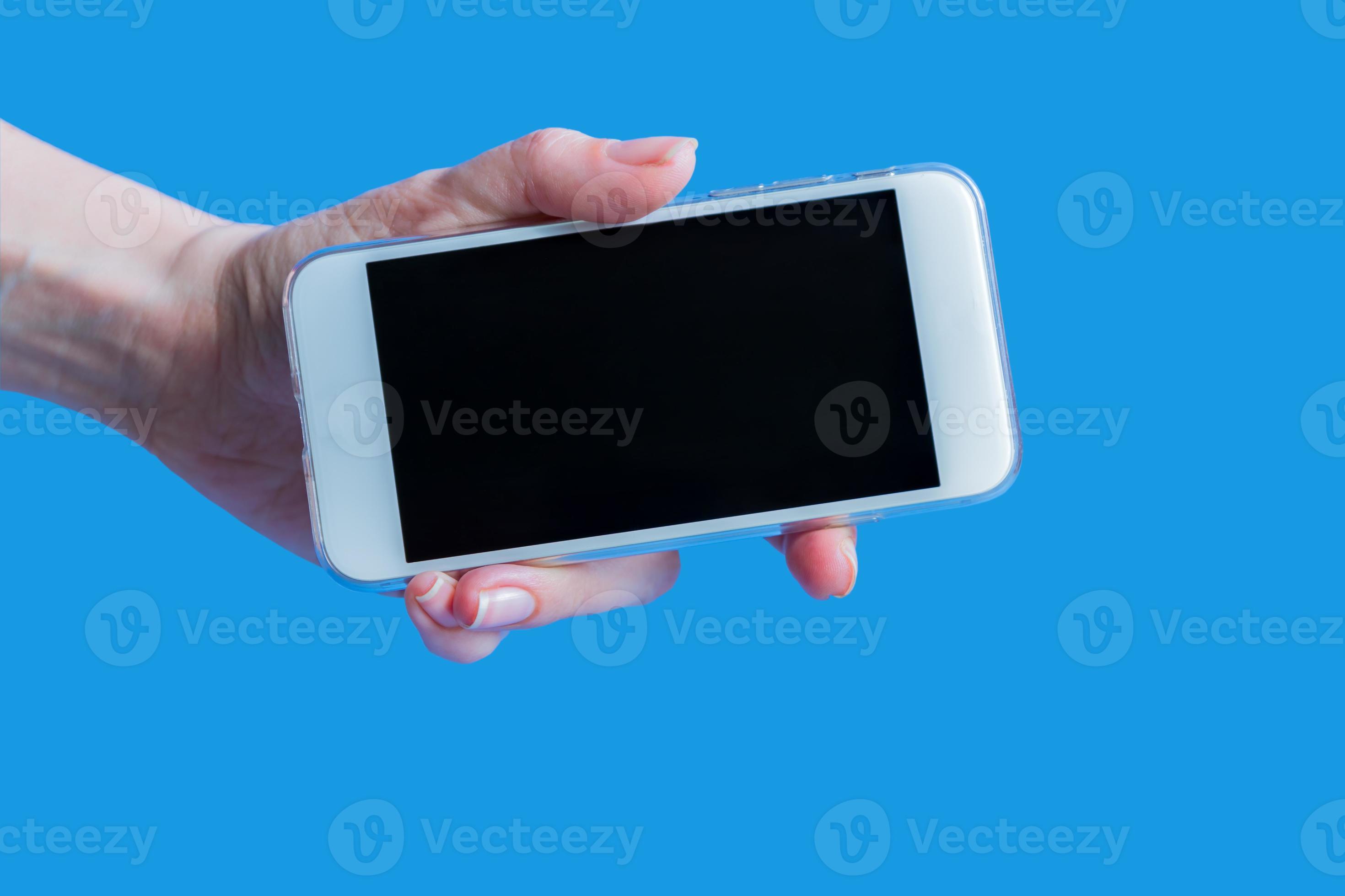 white mobile phone in left female's hand on blue background with copy
