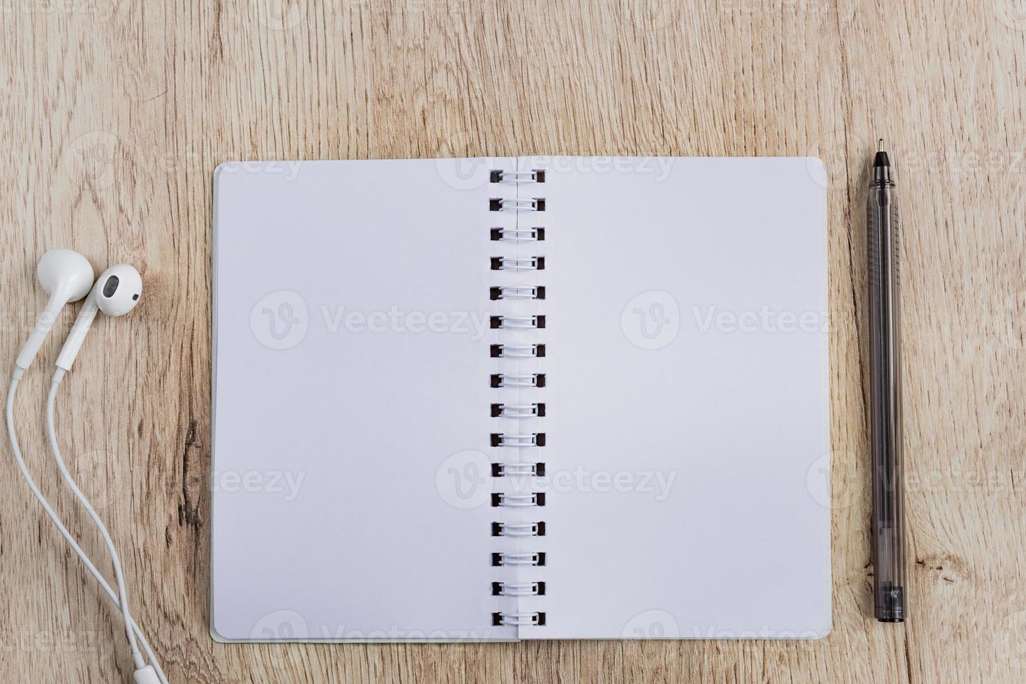 Business and office concept - blank notebook, headphones and black pen on wooden table. Minimal flat lay, top view. photo