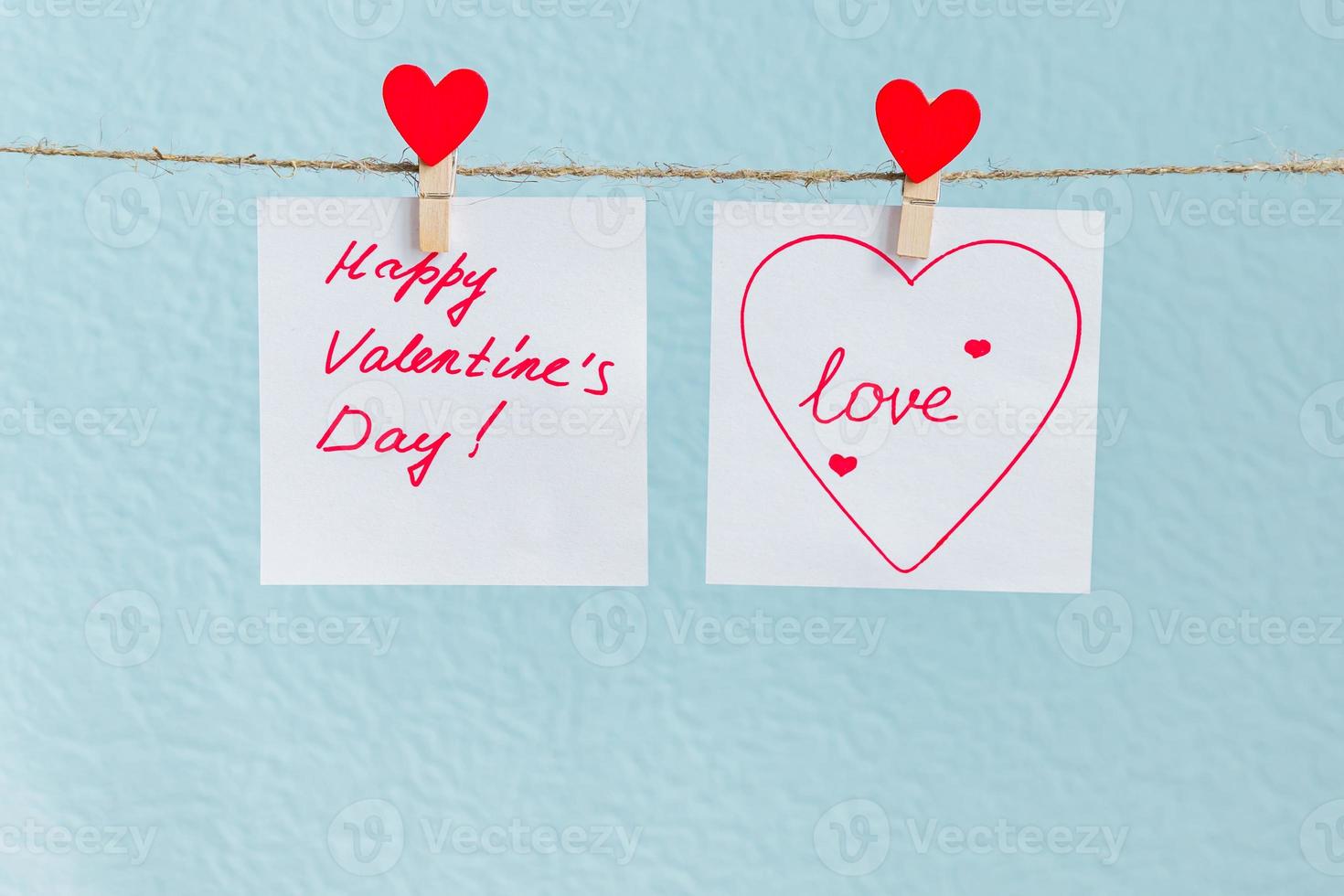 Red Valentine's love hearts pin hanging on natural cord against blue background. drawn heart on paper piece. photo