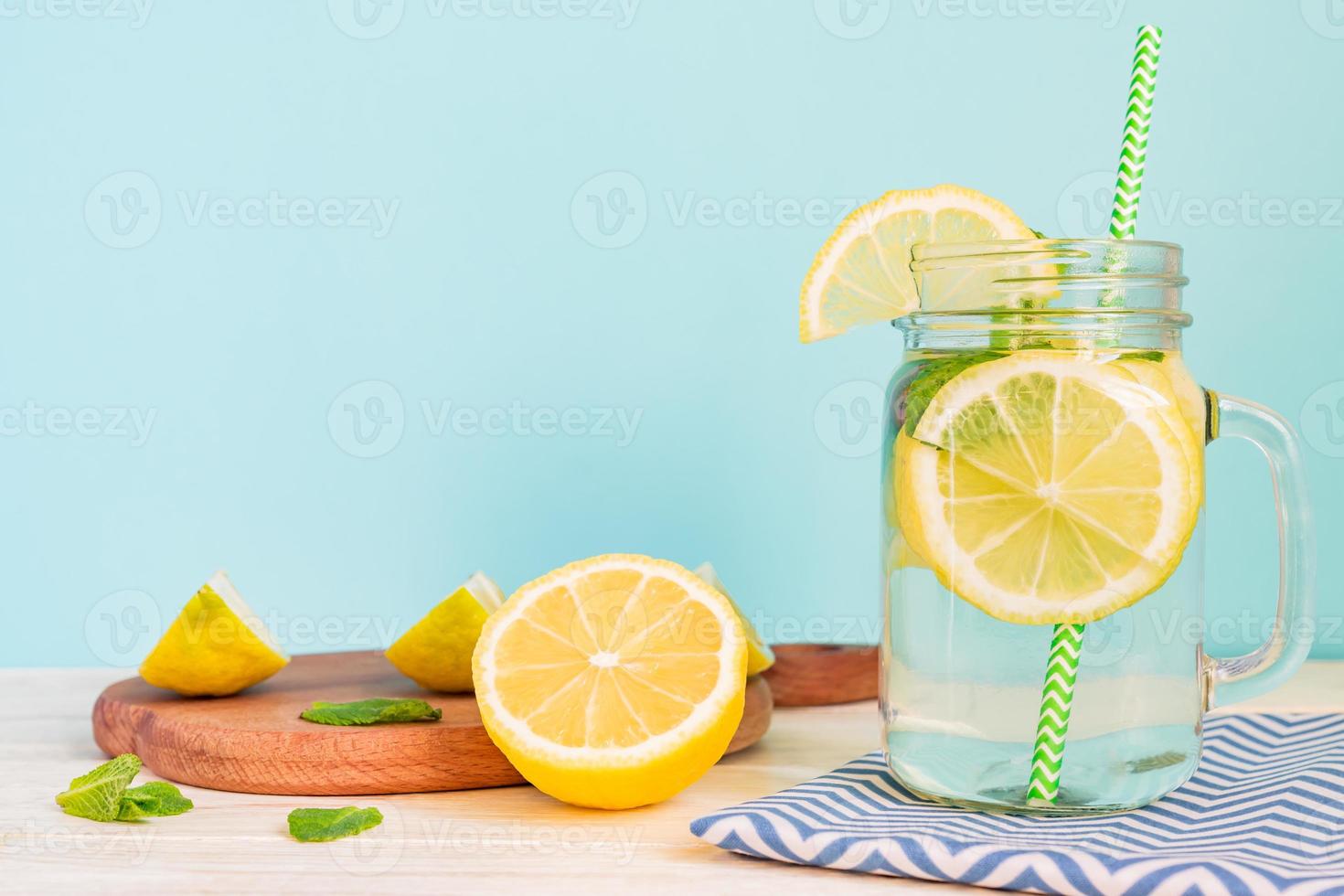 Citrus lemonade water with sliced lemon and mint, healthy and detox water drink in summer on wooden table with blue lighten background photo