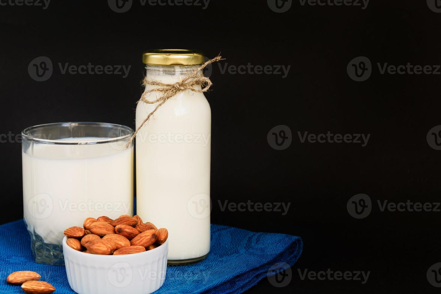 Homemade Almond milk in a bottle and glass with nuts in white porcelain bowl on black background. photo