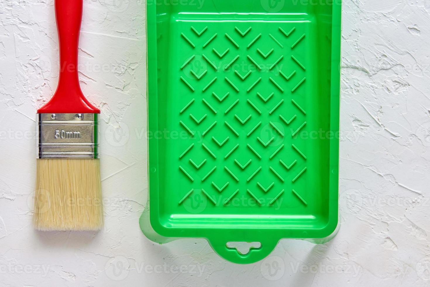 brush with red handle and green paint tray on white concrete background. tools and accessories for home renovation. Top view photo