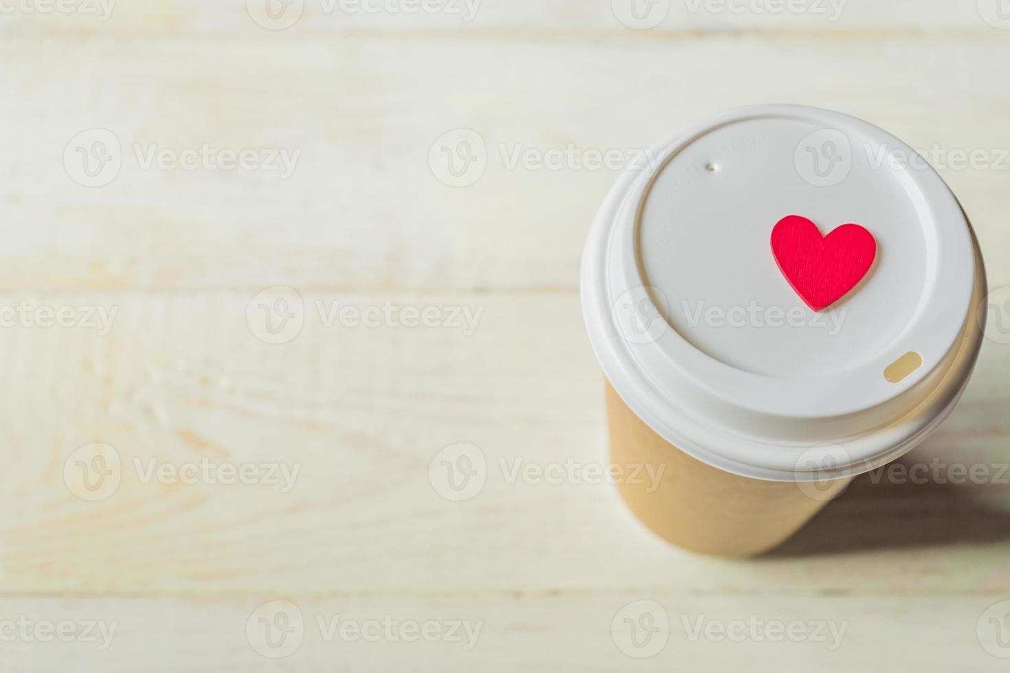 disposable craft paper coffee cup and red wooden heart on a cap. Coff to go on wooden table photo