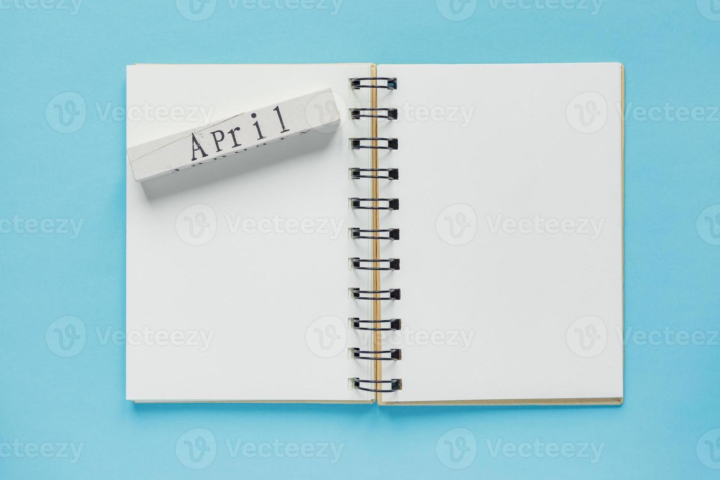 Clean spiral note book for notes and messages and april wooden calendar bar on blue background. Minimal business flat lay photo