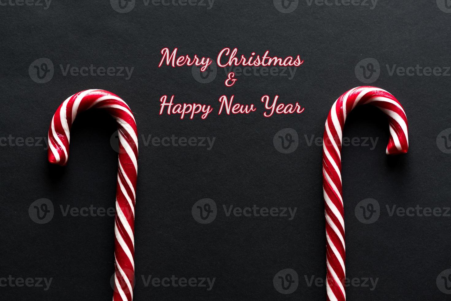 feliz navidad y feliz año nuevo tarjeta de felicitación. dos bastones de caramelo sobre fondo negro foto