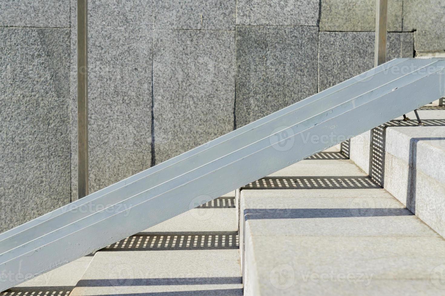 tiled stairs and steel railing ramp for wheelchair, carts and strollers with granite wall and hard sun shadows. Abstract city background photo