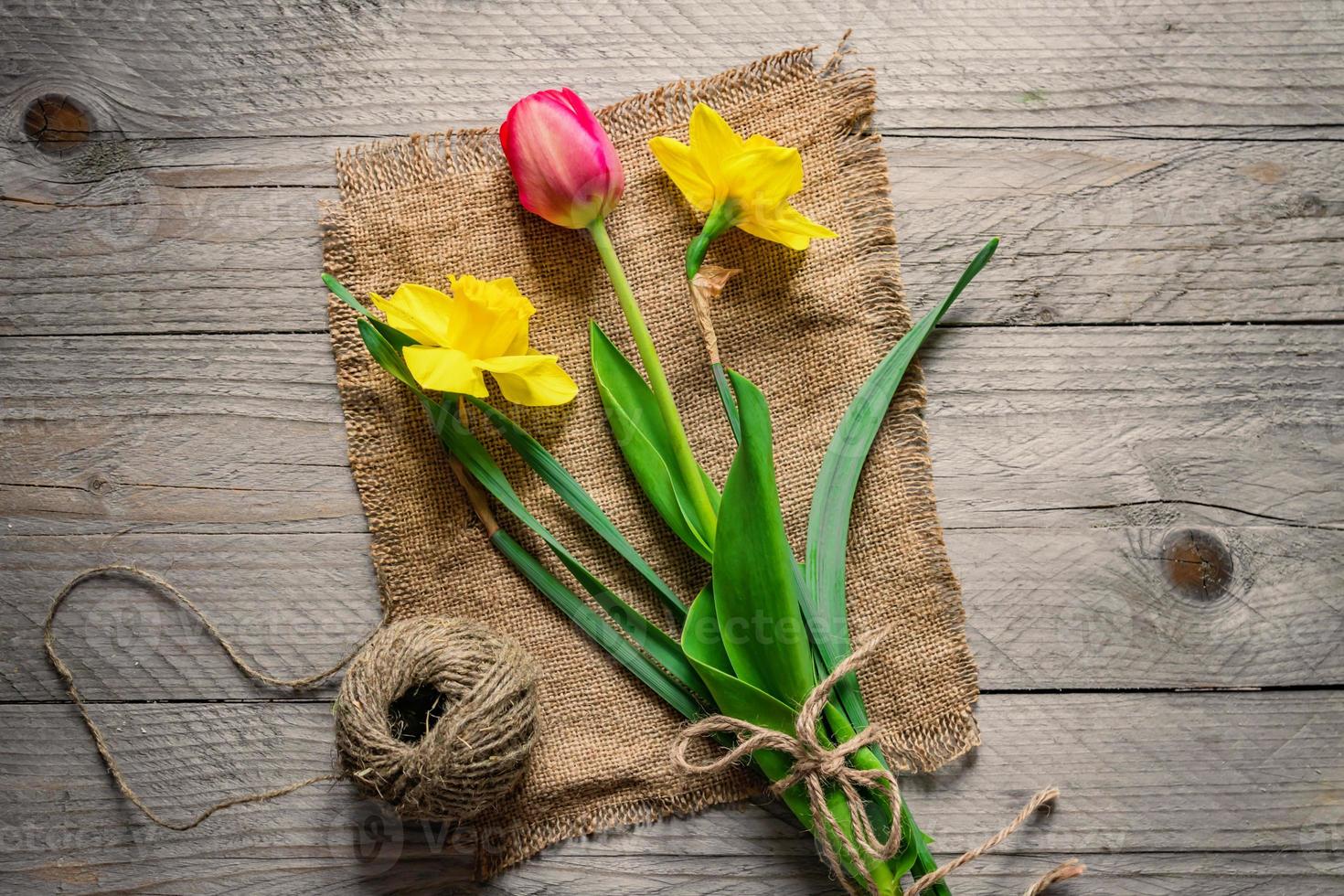 Top view of spring flowers bouquet. Yellow daffodils and pink tulip on wooden background. Copy space. photo