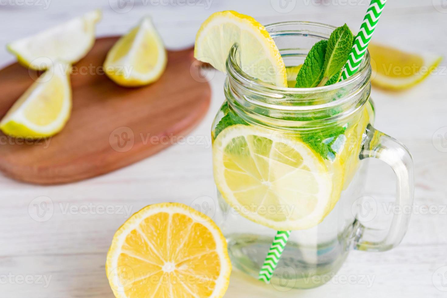 Mason jar glass of homemade lemonade with lemons, mint and green paper straw on wooden rustic background. Summer refreshing beverage. photo