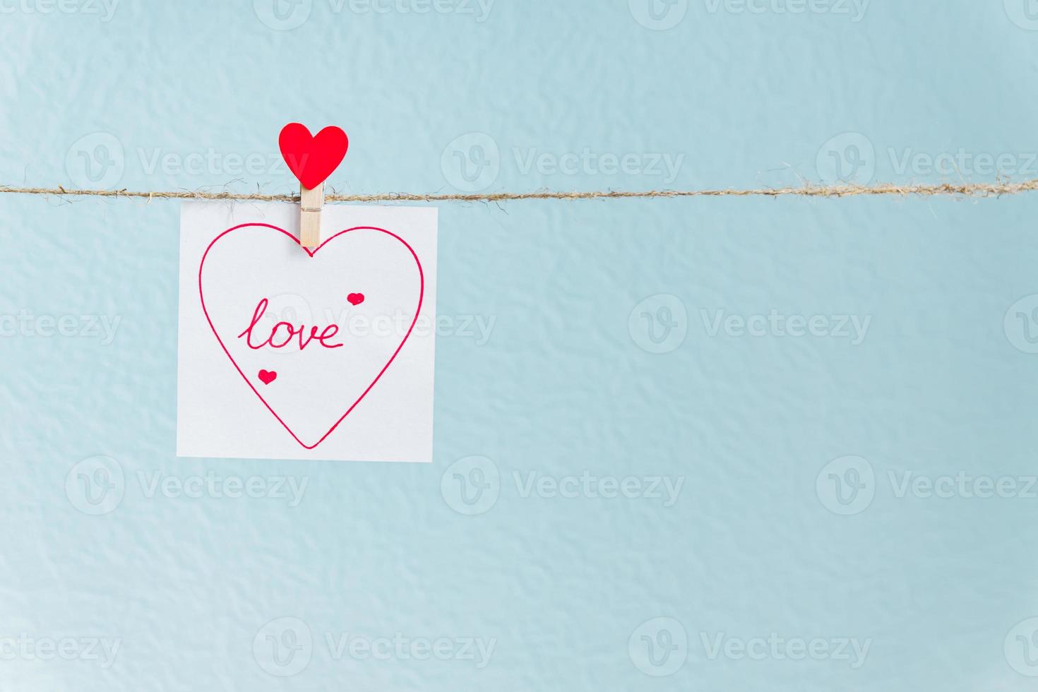 Red Valentine's love heart pin hanging on natural cord against blue background. drawn heart on paper piece. photo