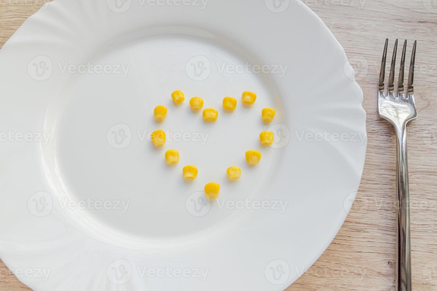 Close up of sweet corn in shape of heart and steel fork on white plate. photo