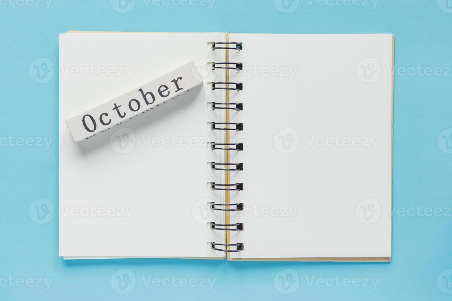 libreta de espiral limpia para notas y mensajes y barra de calendario de madera de octubre sobre fondo azul. plano de negocios mínimo foto