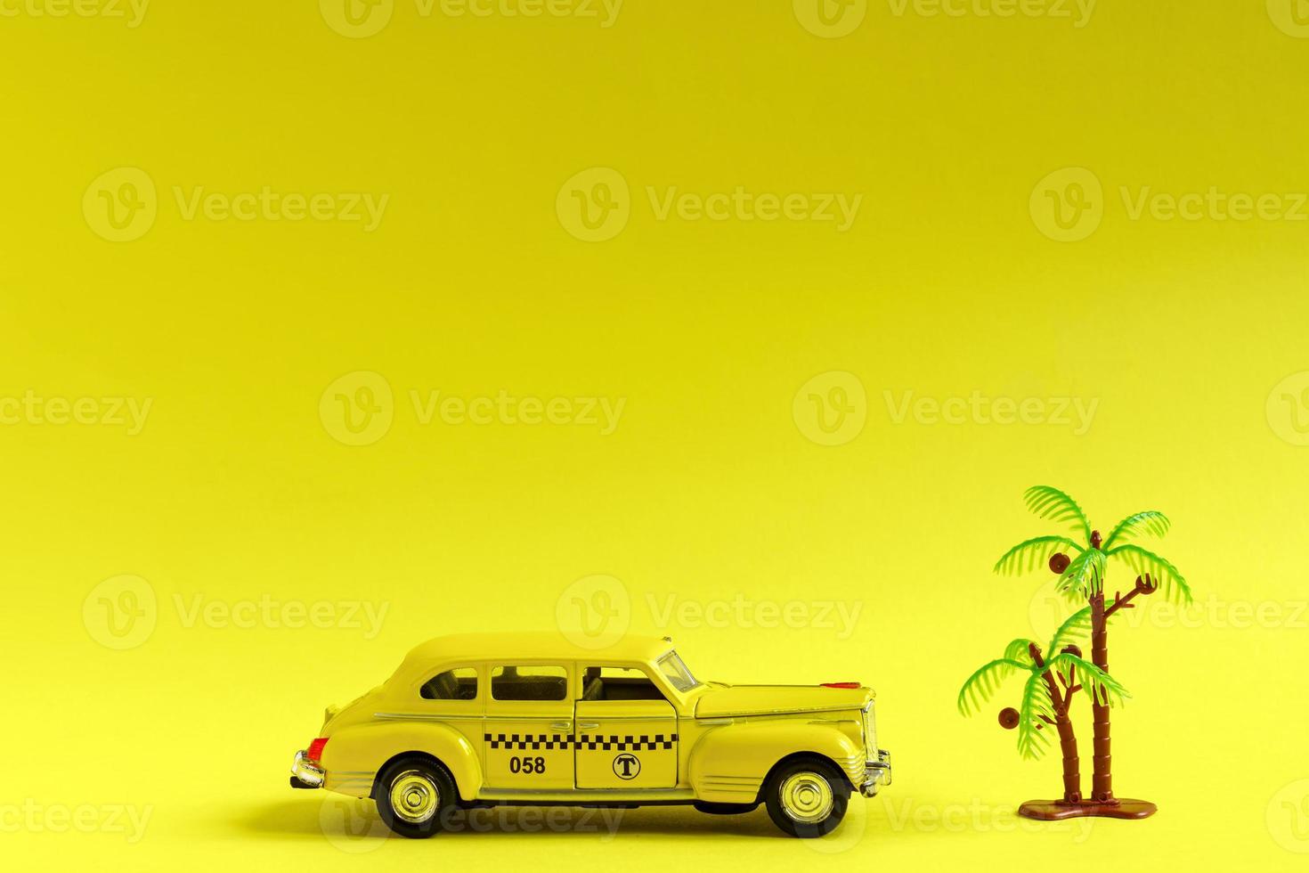 Old retro yellow toy car taxi and toy palm on yellow background with copy space. Travel concept photo