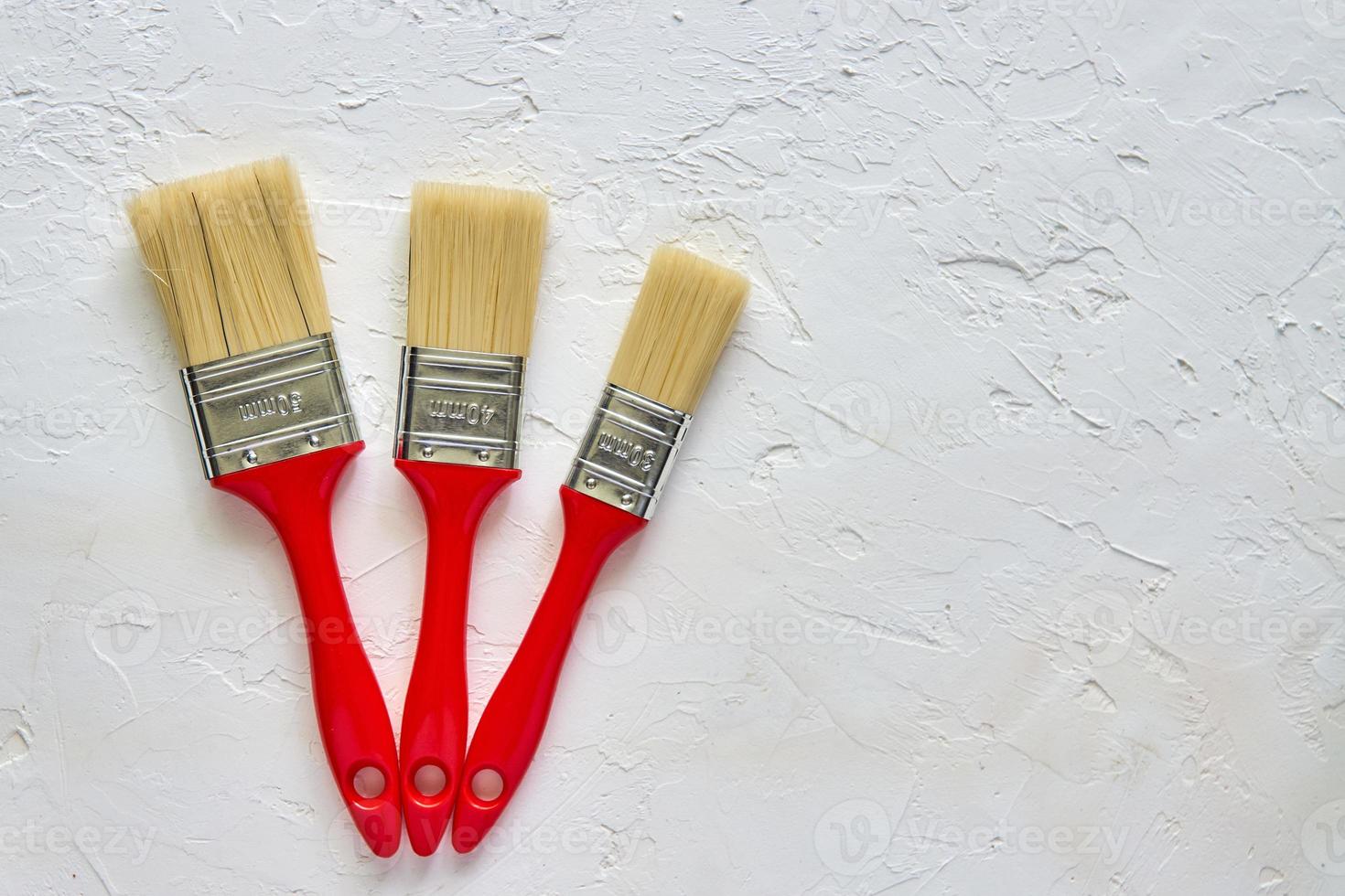 tree paintbrushes with red handles on freshly made concrete background. Repairing concept. Top view with copy space photo