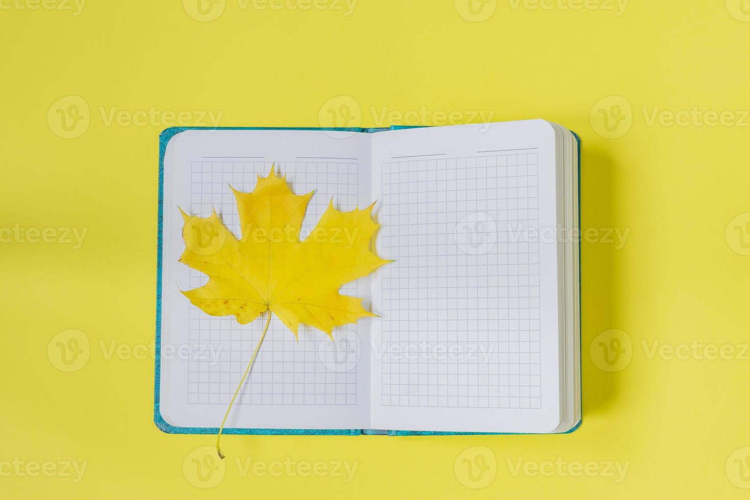 Blank open notebook with maple leaf  on yellow background. Empty diary and autumn concept photo