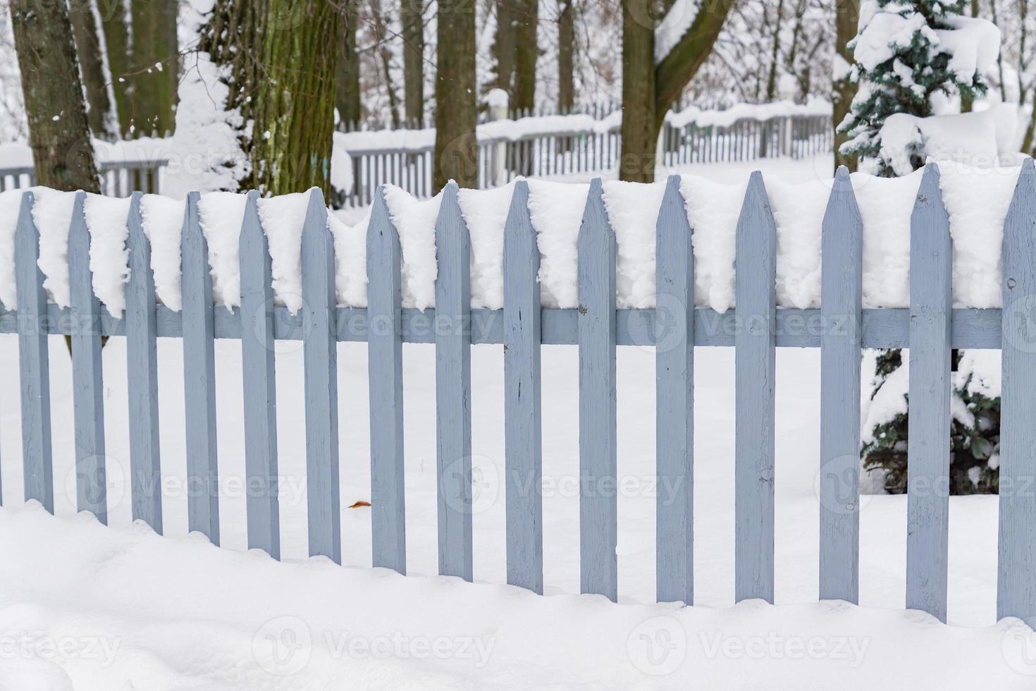 winter in the countryside. Blue wooden fence covered with snow. Snowfall and snowdrift. photo