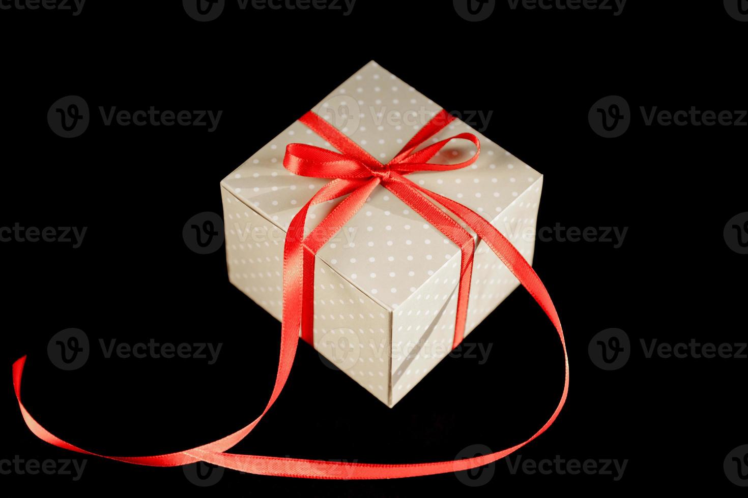 Beige polka dot gift box with red ribbon bow on black background with copy space. photo