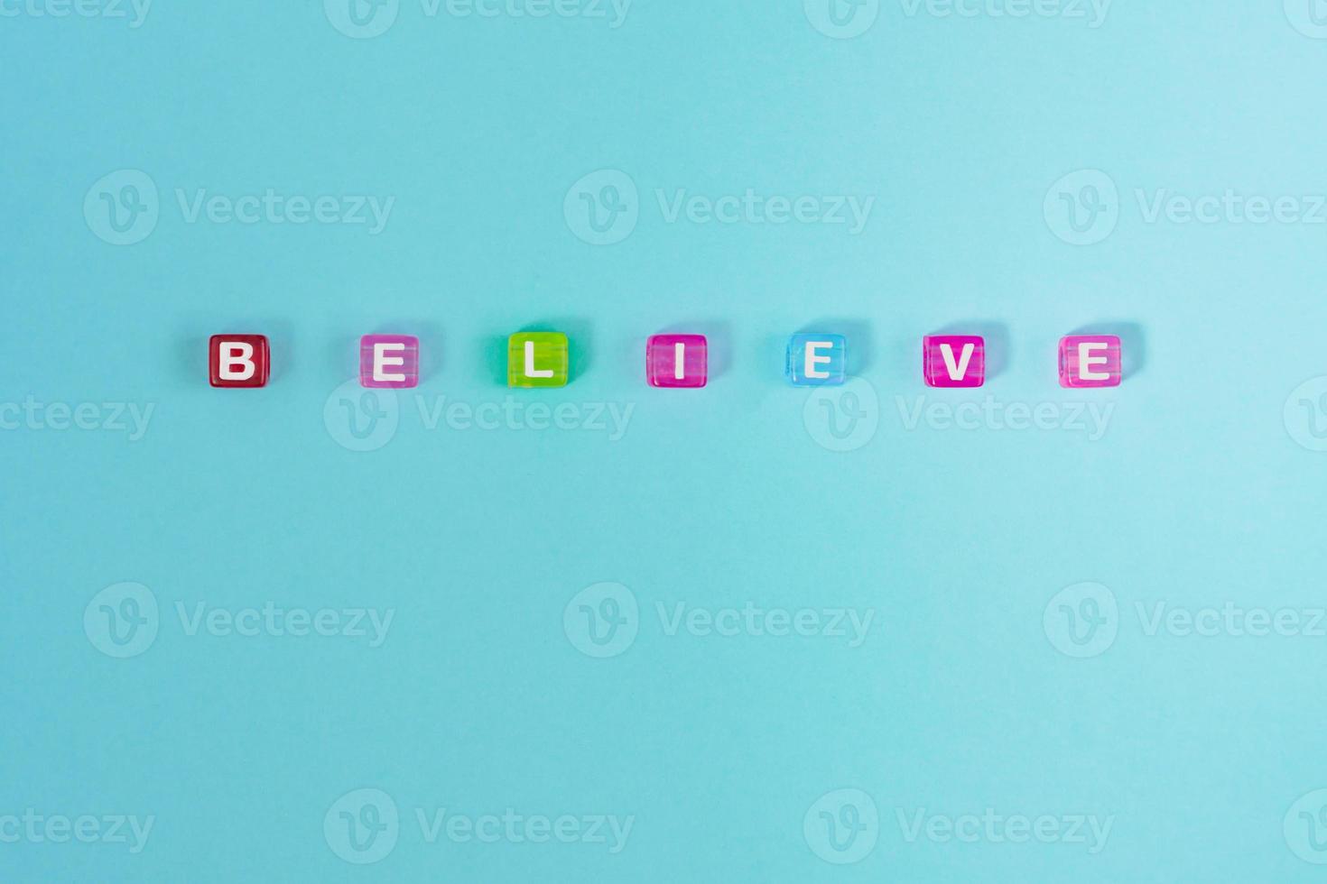 believe inscription made of colorful cube beads with letters. Festive blue background concept with copy space photo