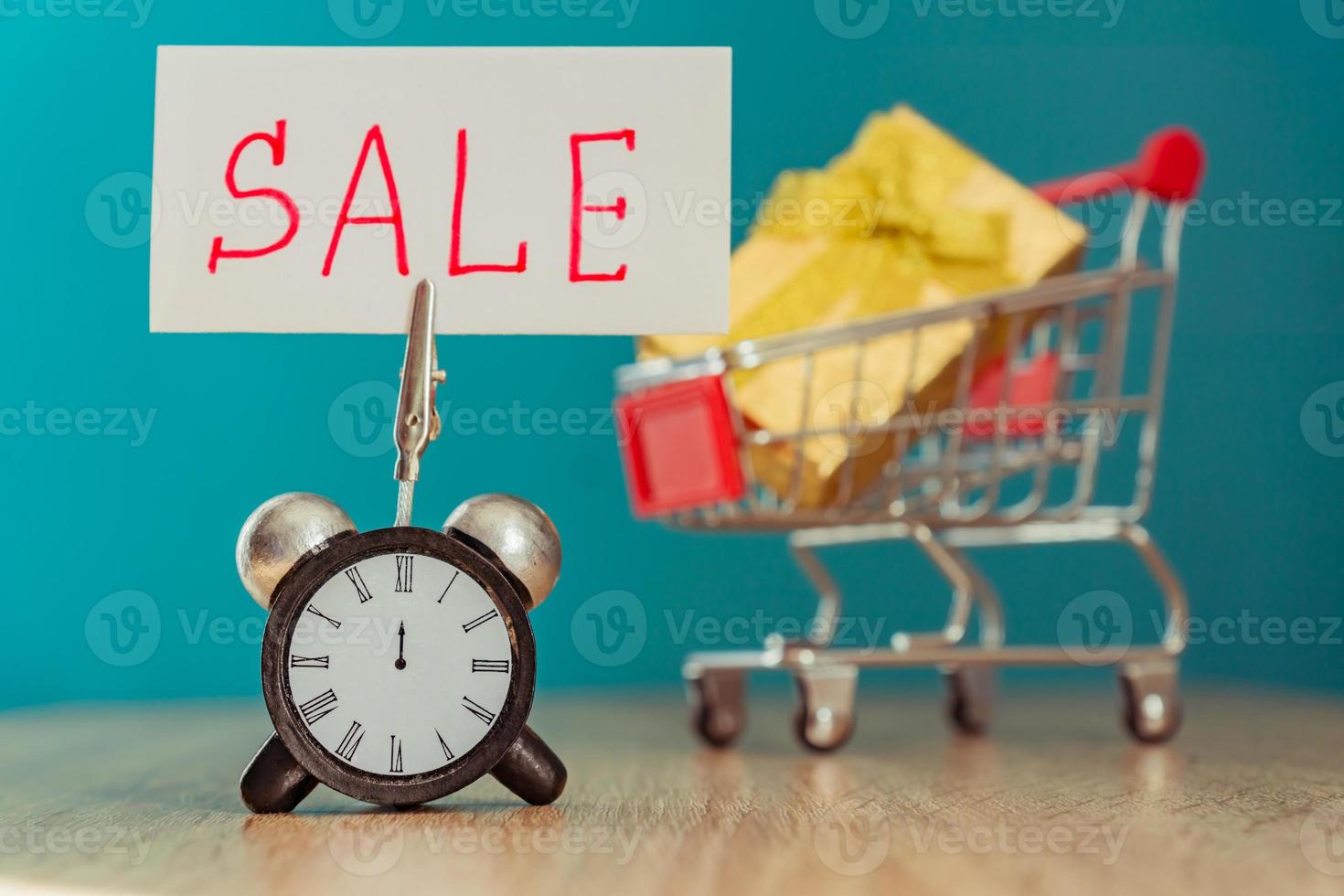 Alarm clock and banner with handwritten world SALE on wooden table. Shopping concept. photo