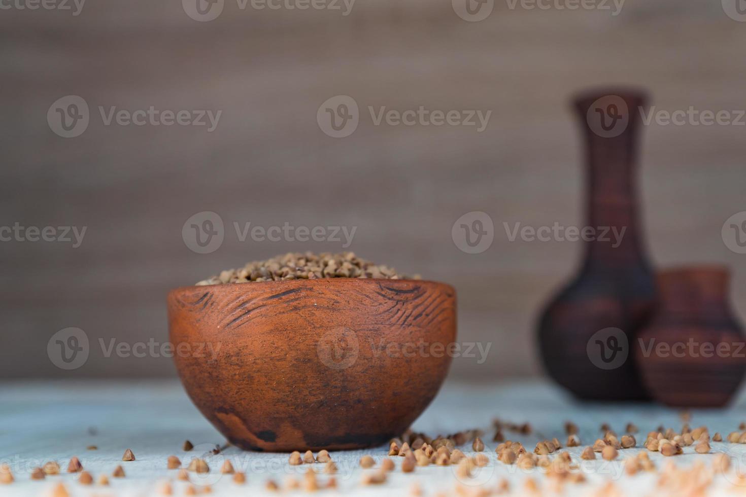 Dry buckwheat in brown clay bowl on wooden table. gluten free grain for healthy diet photo