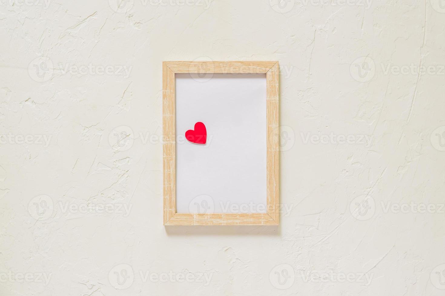 wooden photo frame with red heart on white wall baxkground. Minimal flat lay with copy space