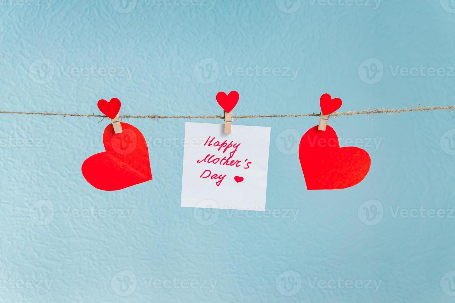 Red love hearts pins hanging on natural cord against blue background. Happy mother's day inscription on piece of paper. photo