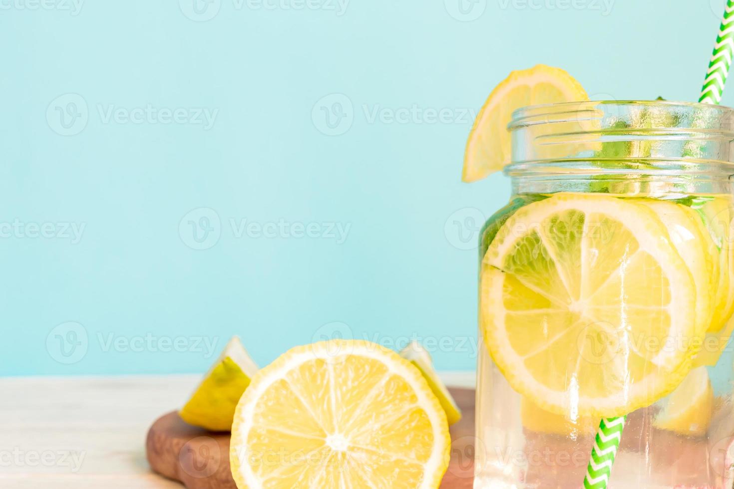 Citrus lemonade water with sliced lemon and mint, healthy and detox water drink in summer on wooden table with blue lighten background photo