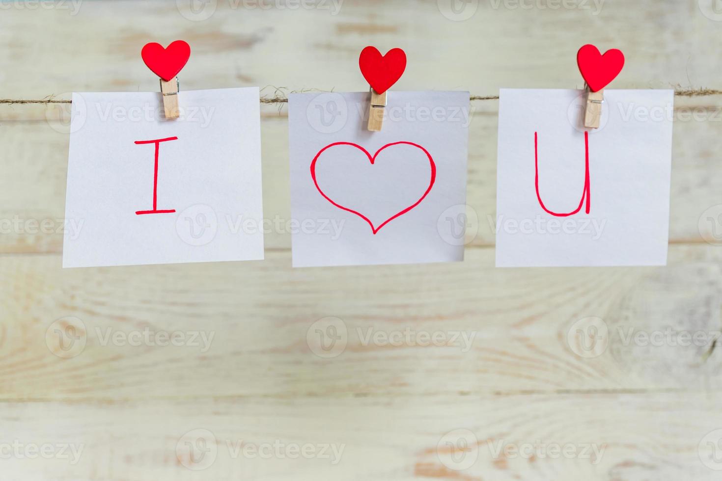 alfileres de corazones rojos de amor de San Valentín colgando de un cordón natural contra un fondo blanco de madera. te amo inscripción en piezas de papel. foto