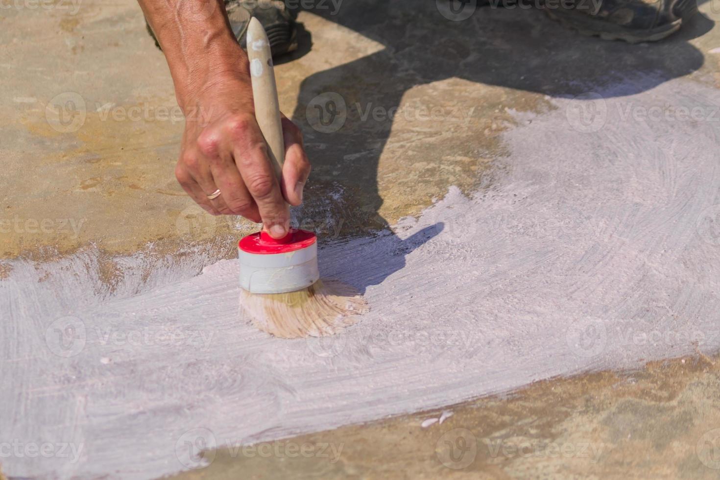 la mano de los trabajadores sostiene un cepillo y pone imprimación en el piso de concreto. reparación y construcción de jardines. foto