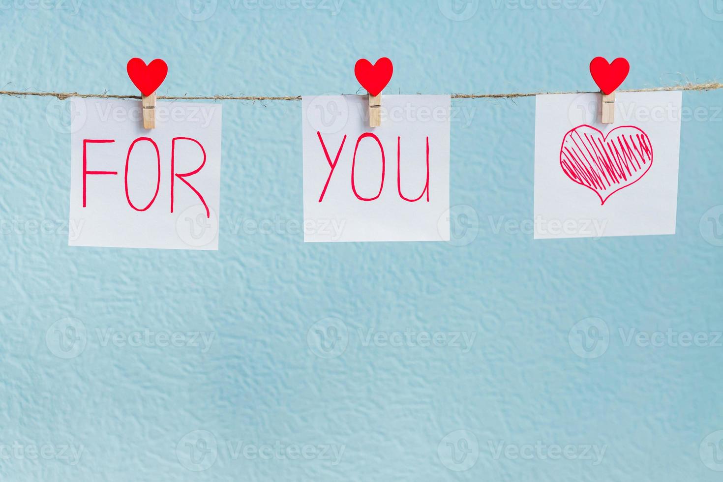 Red Valentine's love hearts pins hanging on natural cord against blue background. love you forever inscription on paper pieces. photo